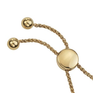 May include: A gold chain bracelet with a round, flat charm and two round beads at the ends. The chain is a rope style.