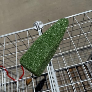 May include: A green, glitter-covered decorative item shaped like a Christmas tree. The item is placed on a metal wire shopping cart. The tree is a solid green color with sparkling glitter throughout.