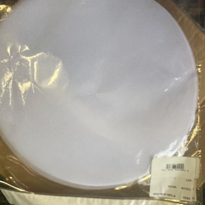 May include: A white, circular fabric item, possibly a hat base or millinery component, is packaged in clear plastic. The fabric has a fine mesh texture. A product label is visible, indicating size and color.