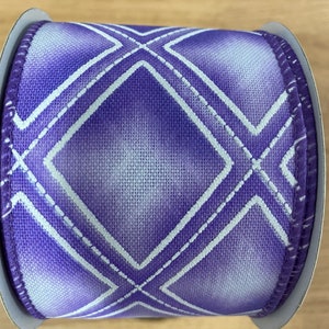 May include: Purple and white ribbon with a diamond pattern. The ribbon is on a spool.