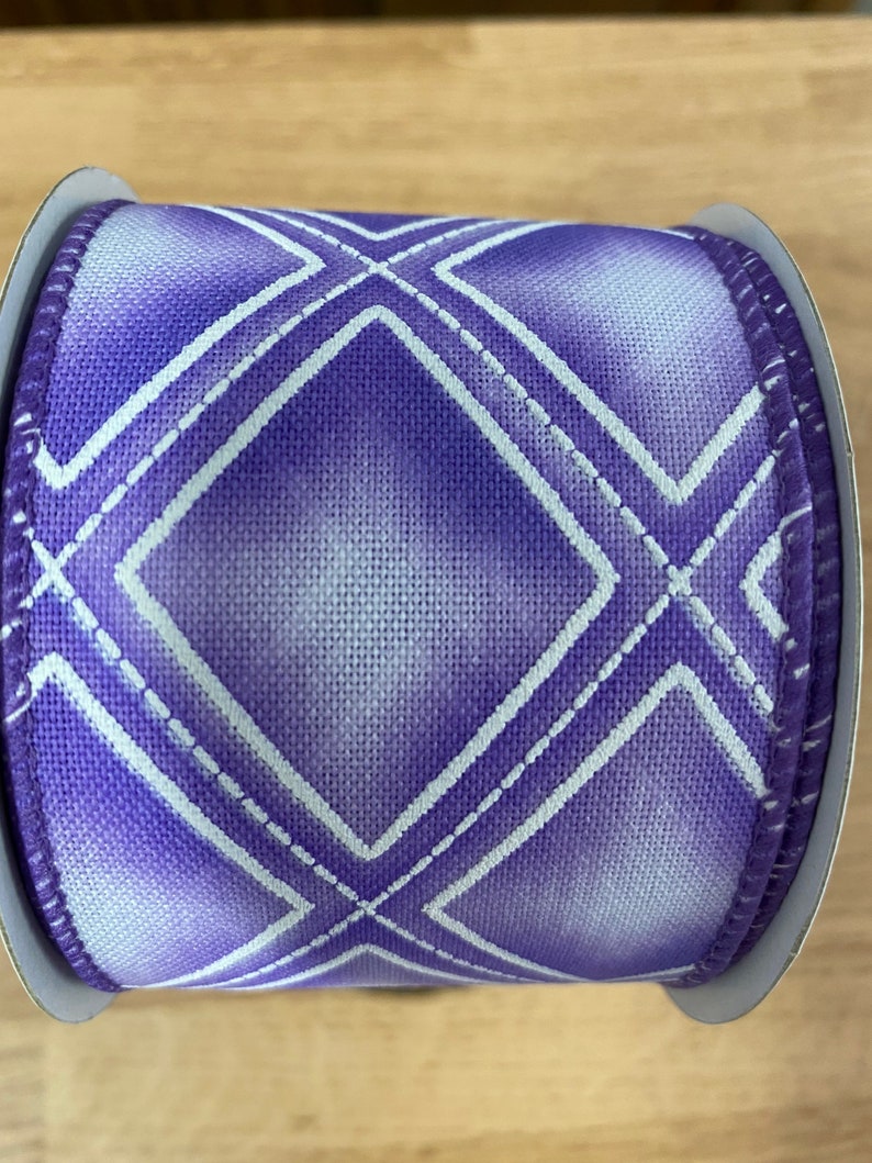 May include: Purple and white ribbon with a diamond pattern. The ribbon is on a spool.