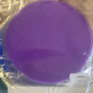 May include: A purple circle of tulle fabric packaged in a clear plastic bag. The bag has a label that reads "Colour: Purple, Code: 10001, Size: 12"