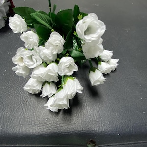 May include: A bouquet of white silk roses with green leaves. The roses are arranged in a cluster and have a realistic appearance.