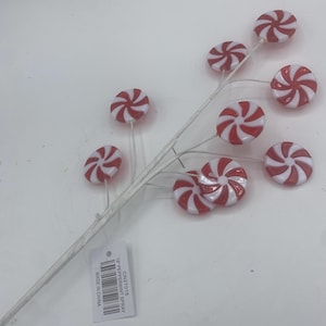 Può includere: Un gambo bianco con ornamenti di caramelle a forma di bastoncino di menta rossa e bianca. L'etichetta riporta "18" Peppermint Spray CN27015 Made in China."