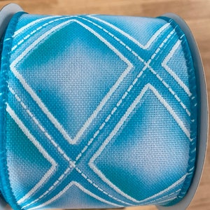 May include: A roll of blue and white ribbon with a diamond pattern. The ribbon is made of a soft, textured fabric and has a subtle ombre effect.