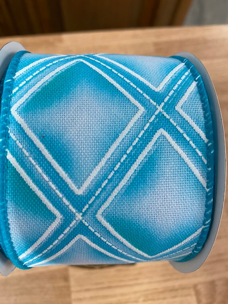 May include: A roll of blue and white ribbon with a diamond pattern. The ribbon is made of a soft, textured fabric and has a subtle ombre effect.
