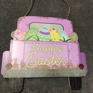 May include: A purple wooden truck with a distressed finish, carrying colorful Easter eggs. The truck has a sign that reads "Happy Easter".