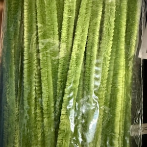 May include: A collection of lime green chenille stems, or pipe cleaners, are seen through a transparent plastic bag. These soft, fuzzy, cylindrical stems are ideal for crafting. The colour is a vibrant, bright green.