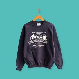 Könnte beinhalten: Ein marineblaues Sweatshirt mit weißem Aufdruck. Der Aufdruck enthält den Text "WHATCOM CHAPTER BACKCOUNTRY HORSEMEN of Washington 20th Anniversary 1986-2006". Das Sweatshirt hängt an einem Holzbügel.