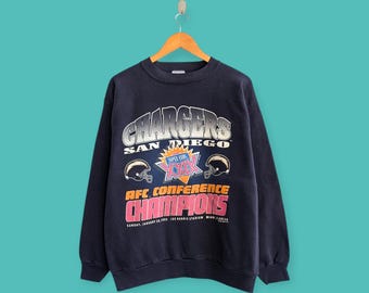 Puede incluir: Sudadera azul marino de los San Diego Chargers. La sudadera presenta el nombre del equipo, logotipos y el texto "AFC Conference Champions" y "Super Bowl XXIX". El texto es en blanco, plata, rojo y rosa.