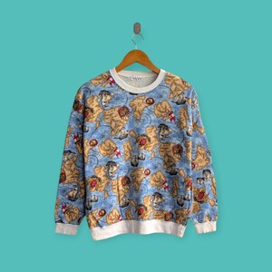 Peut inclure: Un sweat-shirt vintage à col rond avec un motif de carte nautique. Le sweat-shirt présente un fond bleu clair avec un motif répété de cartes anciennes, de boussoles et de voiliers. Le col, les poignets et l'ourlet sont blancs.