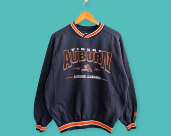 May include: A navy blue sweatshirt with orange and white trim. The front of the sweatshirt has a large orange and white graphic that says "TIGERS AUBURN AUBURN, ALABAMA".