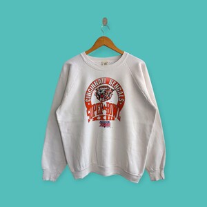 May include: White vintage sweatshirt with an orange and white graphic of the Cincinnati Bengals Super Bowl XXIII logo. The logo features a tiger head with the words "Cincinnati Bengals Super Bowl XXIII" around it.