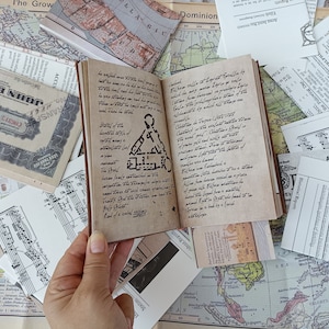 May include: A vintage-style journal with handwritten text and a geometric illustration, held over a backdrop of old maps and documents. The journal's pages are aged, and the cover is brown.