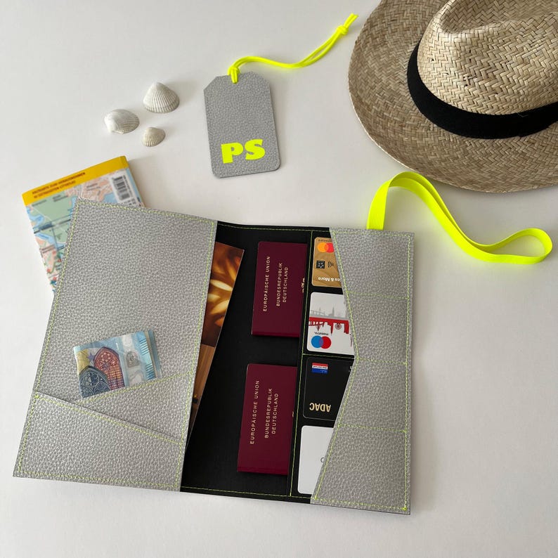 May include: A gray leather travel wallet with multiple pockets and slots for holding passports, credit cards, and cash. The wallet is open and has a bright yellow strap.