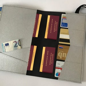 May include: A gray leather travel wallet with multiple pockets and a strap. The wallet is open and shows a passport, credit cards, and cash.