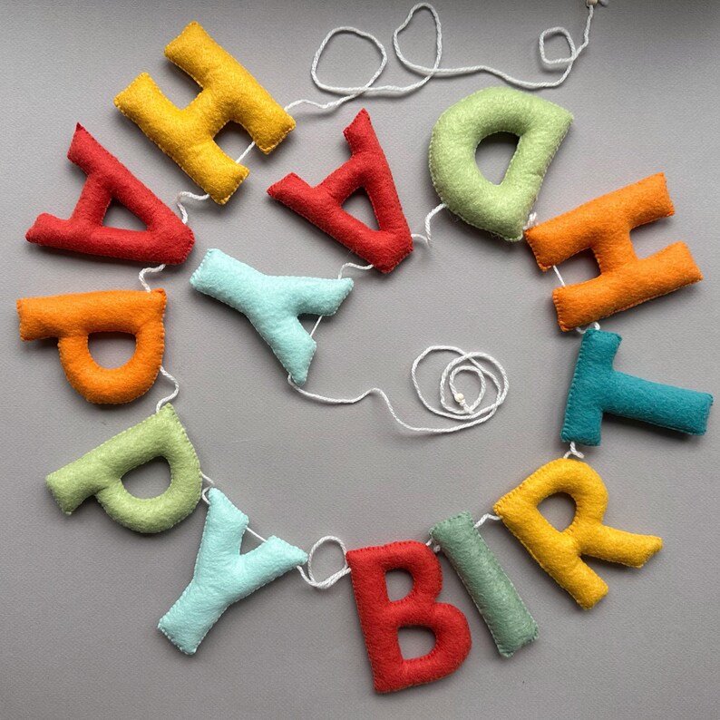 May include: A colorful felt banner with the word "Happy Birthday" spelled out in individual letters. The letters are strung together with white twine.