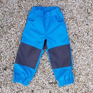 Op de afbeelding: Blauwe en grijze kinderbroek met elastische tailleband en zijzakken.