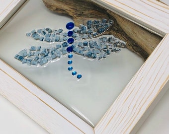 May include: A white wood framed picture with a blue and silver mosaic dragonfly inside. The dragonfly has blue rhinestones on its body.