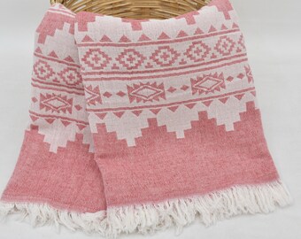 Puede incluir: Una toalla turca de color rosa y blanco con flecos. La toalla está doblada y colocada sobre una cesta de mimbre.