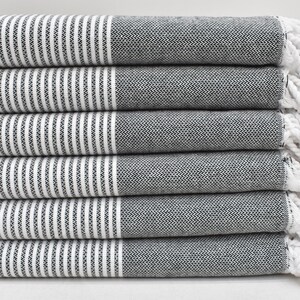 May include: A stack of six black and white striped towels with white fringe. The towels are folded and stacked neatly.