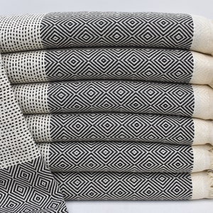 May include: A stack of six black and white patterned Turkish towels with fringe. The towels are folded and stacked on a white surface.
