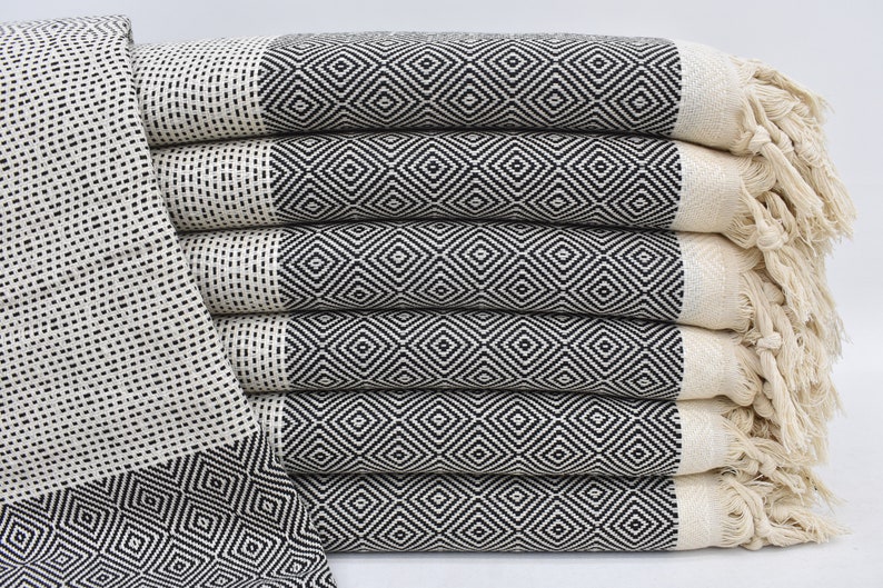May include: A stack of six black and white patterned Turkish towels with fringe. The towels are folded and stacked on a white surface.