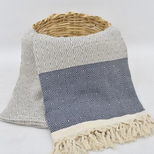 May include: A white and blue patterned throw blanket with fringe. The blanket is folded and draped over a wicker basket.