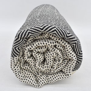May include: A rolled up black and white patterned Turkish towel. The towel is made of cotton and has a geometric design.