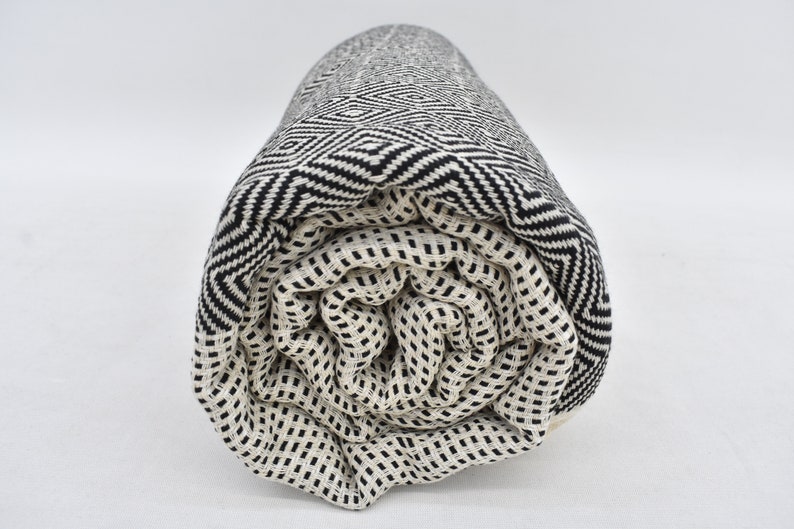 May include: A rolled up black and white patterned Turkish towel. The towel is made of cotton and has a geometric design.