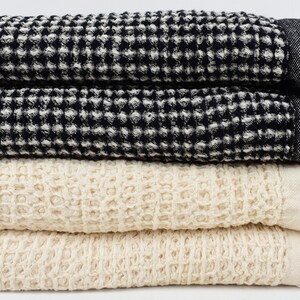 May include: A stack of four waffle weave towels in black and white and cream. The towels have a textured waffle weave pattern and are folded neatly.