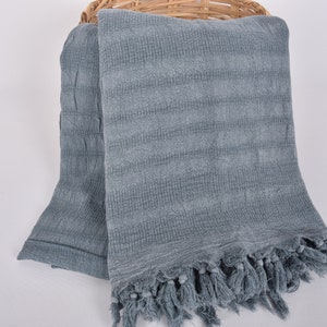May include: A soft, blue, woven throw blanket with a fringe border. The blanket is folded and draped over a wicker basket.