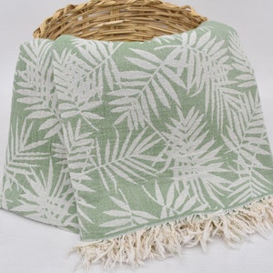 May include: A green and white patterned beach towel with fringe. The towel features a white leaf design on a light green background.