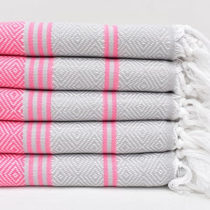 May include: A stack of five grey and pink striped towels with white fringe. The towels have a diamond pattern.