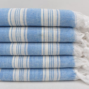 May include: A stack of five blue and white striped towels with white fringe. The towels are folded and stacked on a white surface.
