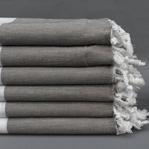 May include: A stack of six gray and white striped towels with white fringe. The towels are folded and stacked on a gray surface.