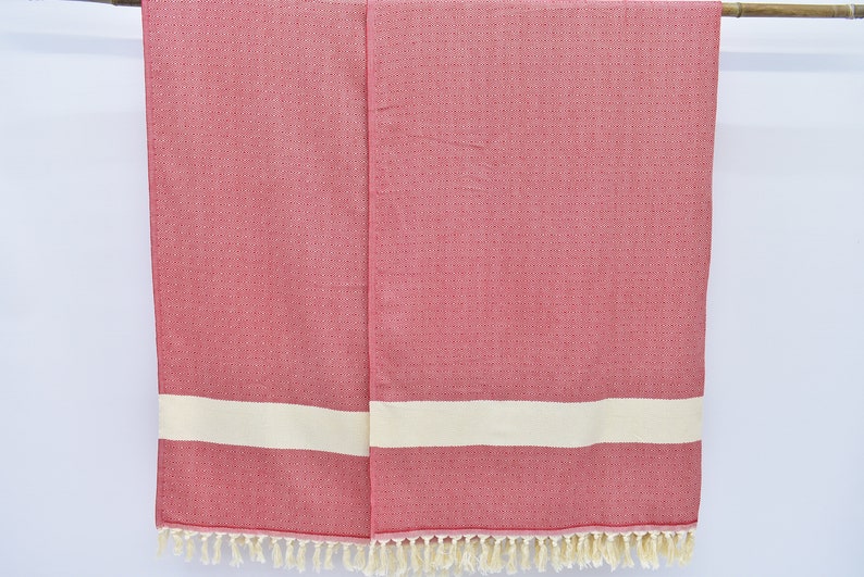 May include: Two red and white striped towels with fringe on the bottom. The towels are hanging on a wooden rod.