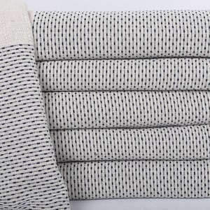 Puede incluir: Una pila de seis toallas turcas color crema con un patrón azul marino punteado. Las toallas tienen un borde con flecos y un borde liso color crema. Las toallas están dobladas cuidadosamente, mostrando la textura y el diseño.