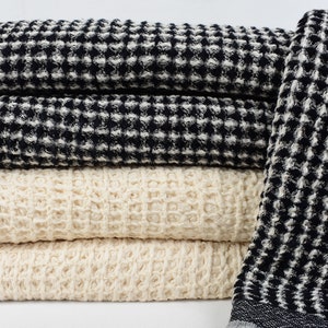 May include: A stack of waffle weave towels in black and white and natural colors. The towels are folded and arranged in a pile.