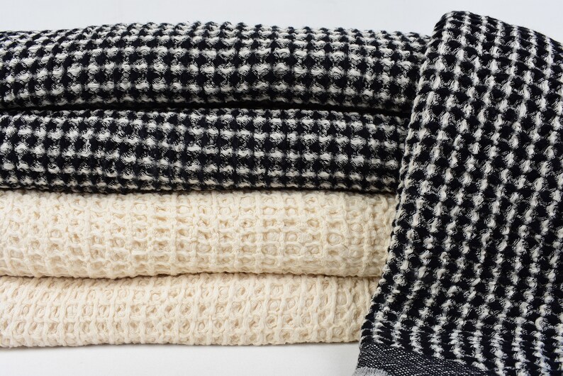 May include: A stack of waffle weave towels in black and white and natural colors. The towels are folded and arranged in a pile.