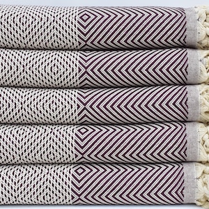 May include: A stack of five woven cotton towels. Each towel features a geometric diamond pattern in cream and burgundy. The towels have fringed edges and are folded neatly, showcasing the intricate design and texture.