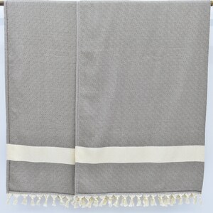 May include: Two gray towels with white stripes and fringe trim hanging on a wooden rod.
