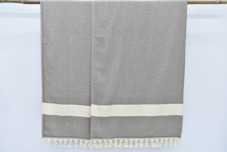 May include: Two gray towels with white stripes and fringe trim hanging on a wooden rod.