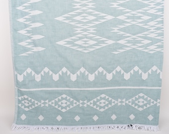May include: A light blue beach towel with a white geometric pattern. The towel has a fringe border.