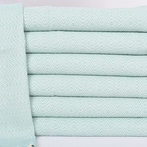 May include: A stack of light blue Turkish towels with a diamond pattern and white fringe.