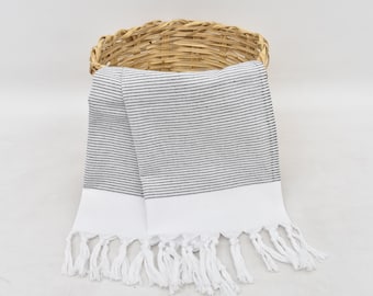 May include: Two white kitchen towels with black stripes and white fringe. The towels are folded and placed in a wicker basket.