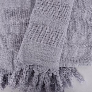 May include: A gray woven throw blanket with fringe on the edges. The blanket is folded in half and has a textured pattern.