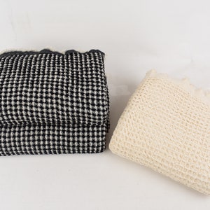 May include: Two waffle weave blankets, one black and white and one cream. The blankets are folded and placed on a white surface.
