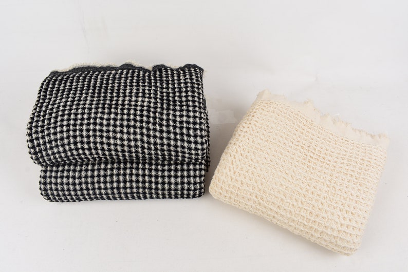 May include: Two waffle weave blankets, one black and white and one cream. The blankets are folded and placed on a white surface.