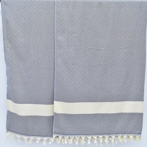 May include: Two gray towels with white stripes and fringe. The towels are hanging on a wooden rod.